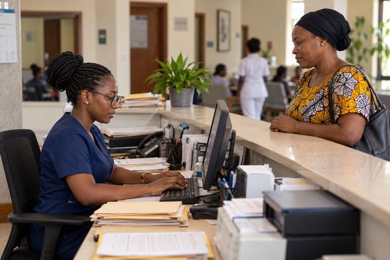 A clinic receptionist types a patient’s details into a computer while the patient waits at the counter